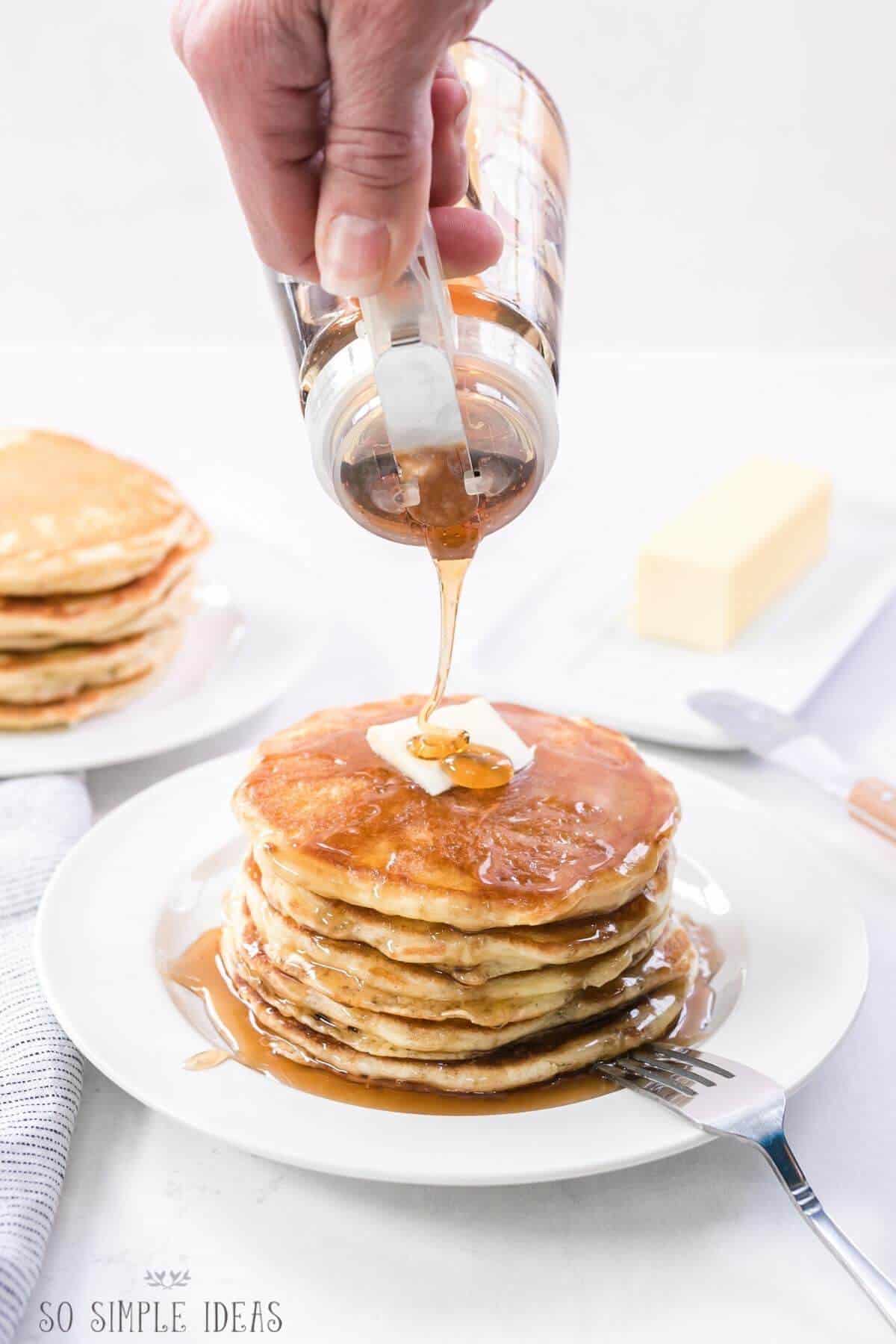 pouring maple syrup over stack of pancakes