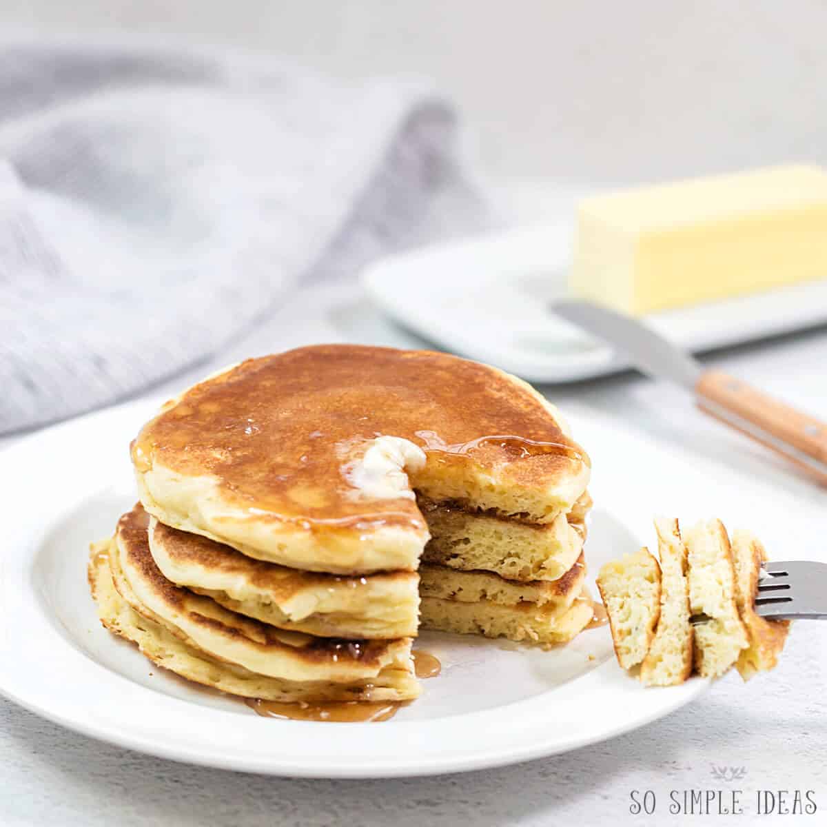 stack of pancakes on white plate with butter and syrup with fork bite