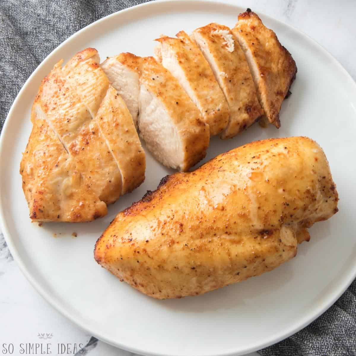 cooked chicken breasts on white plate with one sliced.