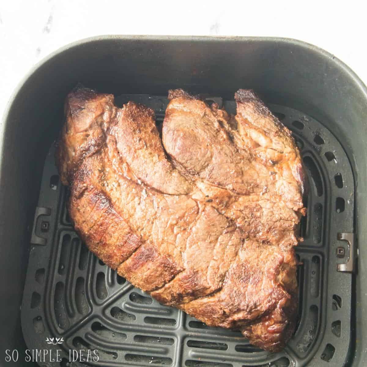 cooked roast beef in air fryer basket.