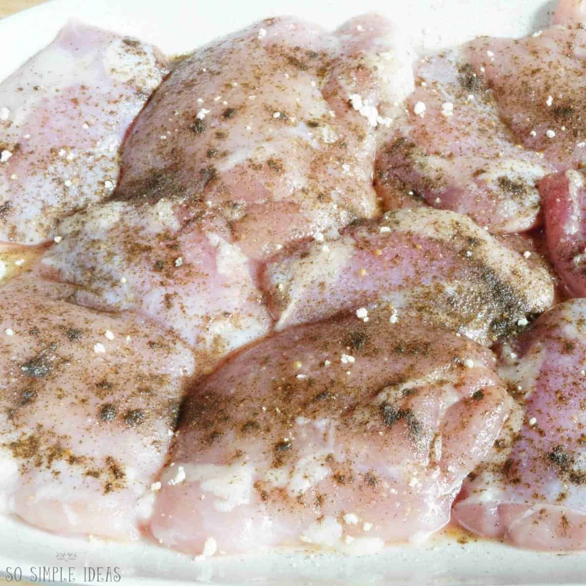 raw boneless chicken thighs seasoned on plate.