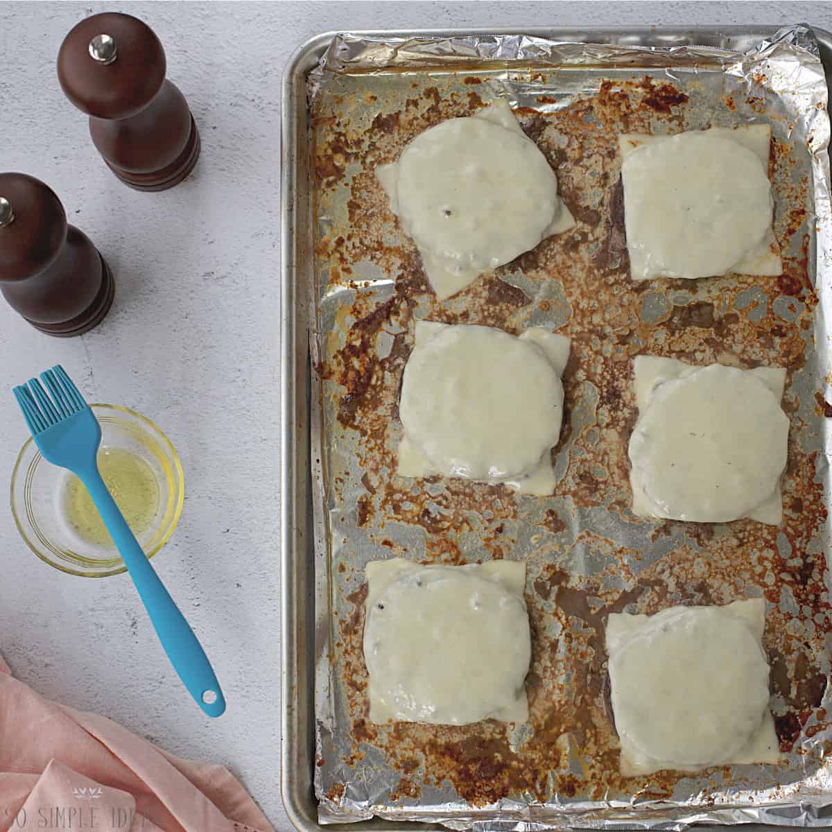 baked cheeseburgers on lined baking sheet..