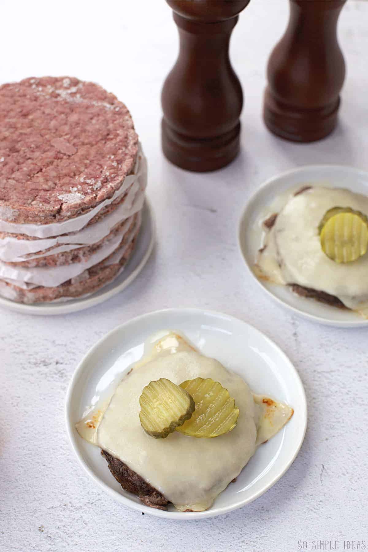 bun-less cheeseburgers on small white plates with frozen hamburger patties.