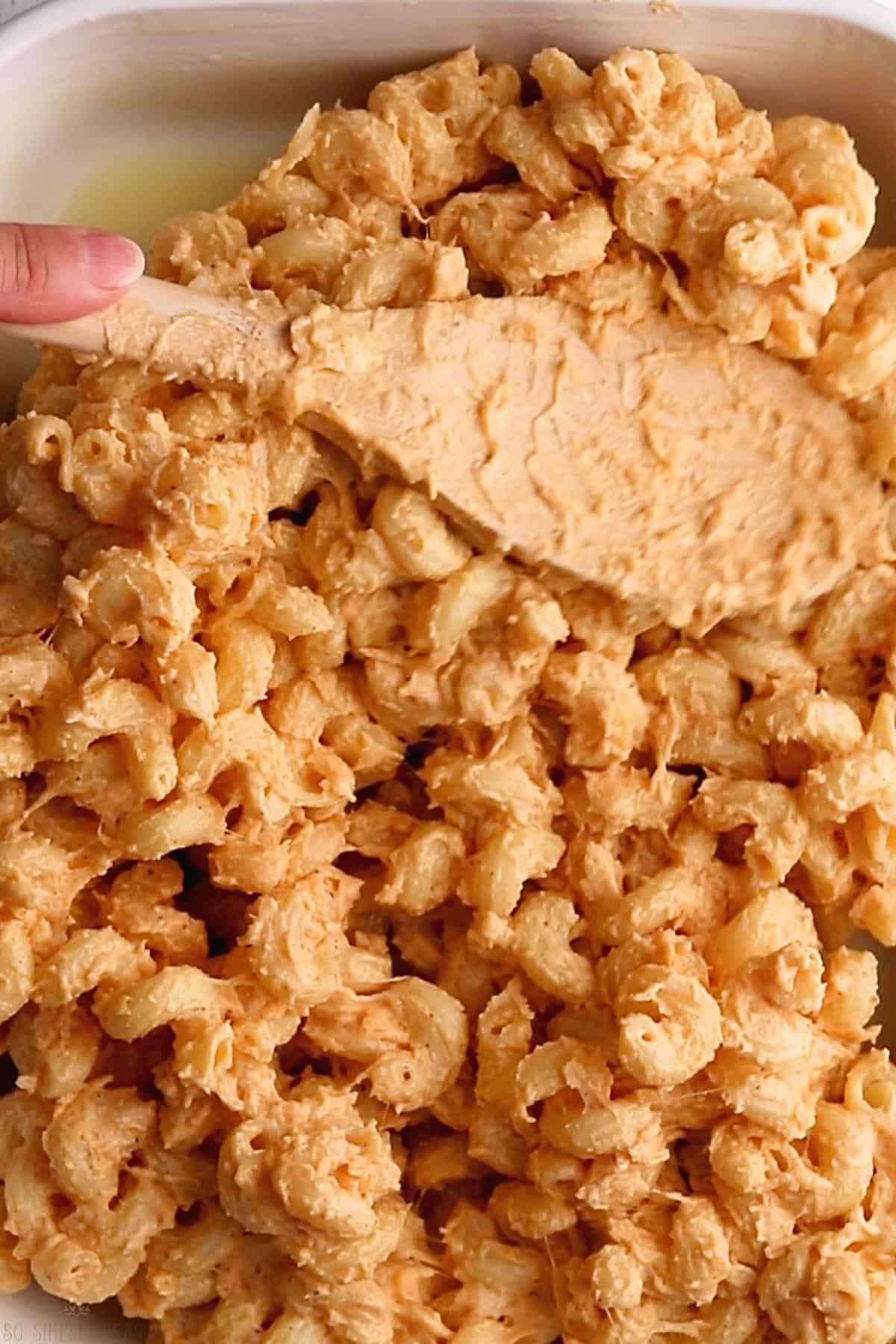 spreading mac and cheese pasta mixture into buttered casserole pan.