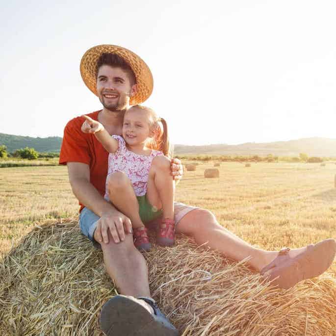 farmer and girl on rock in hay field.