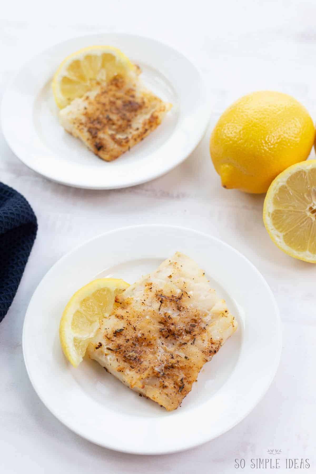cooked fish fillets on white plates with lemon.