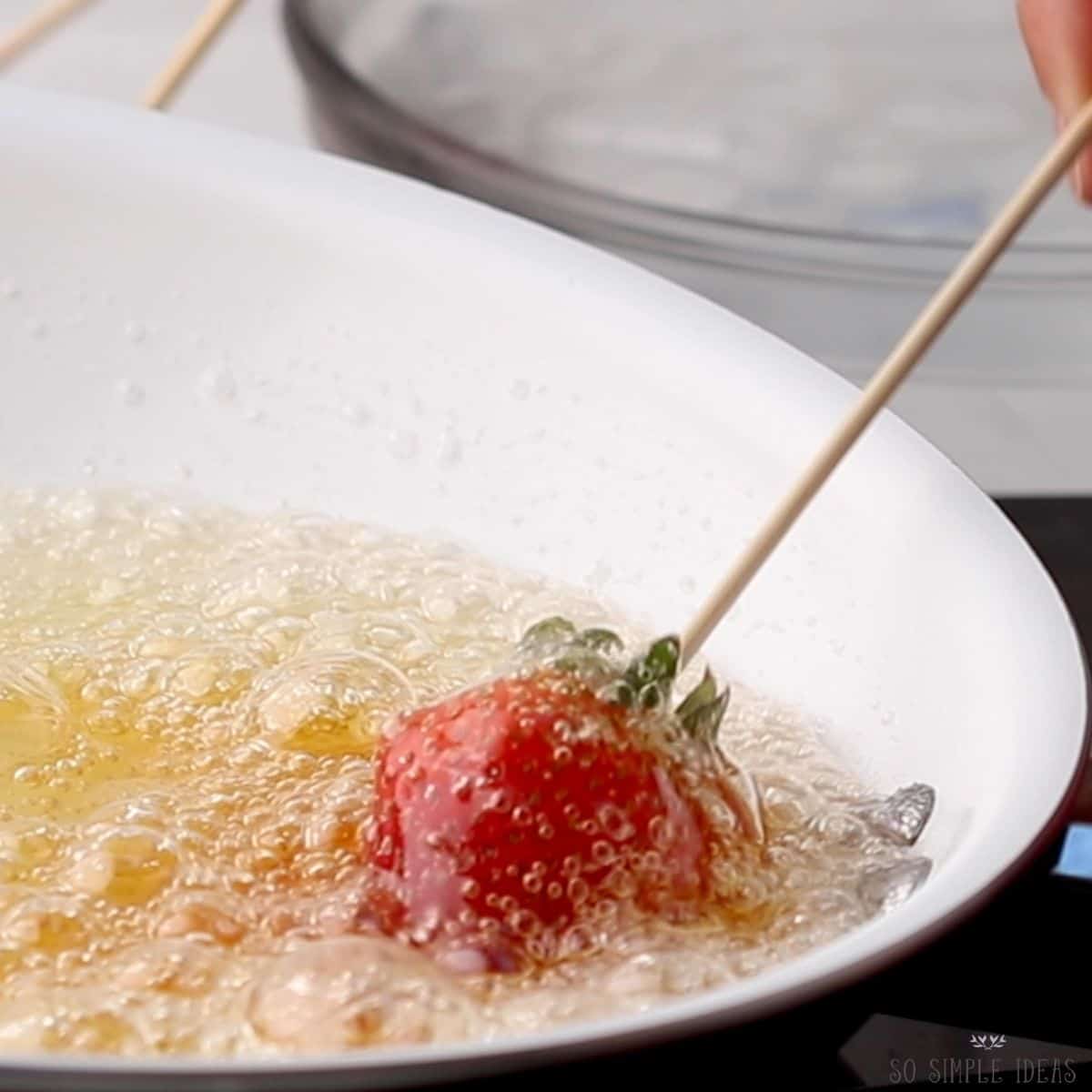 dipping skewered strawberry in hot candy syrup.