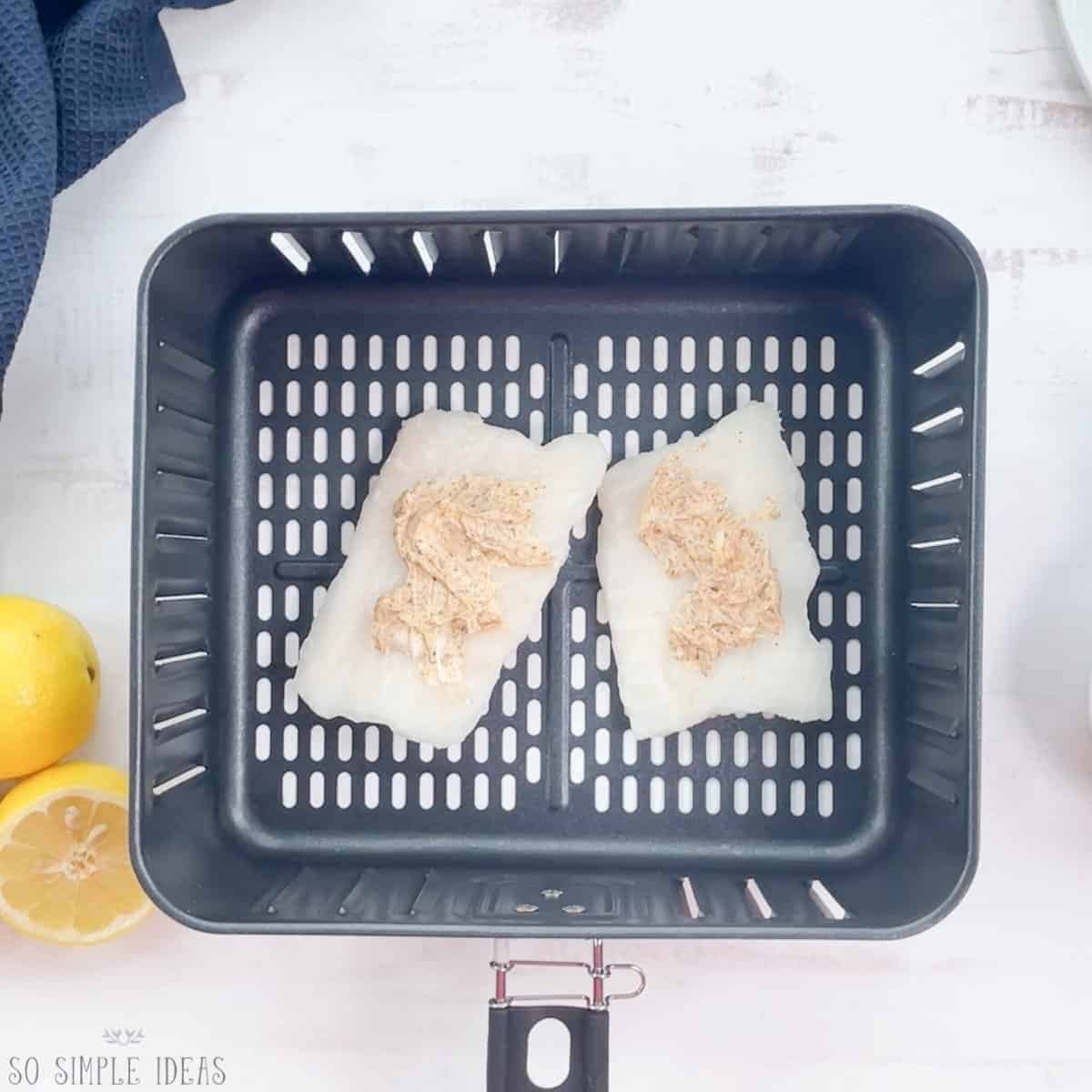 frozen fish fillets in air fryer basket with seasoned butter spread over.