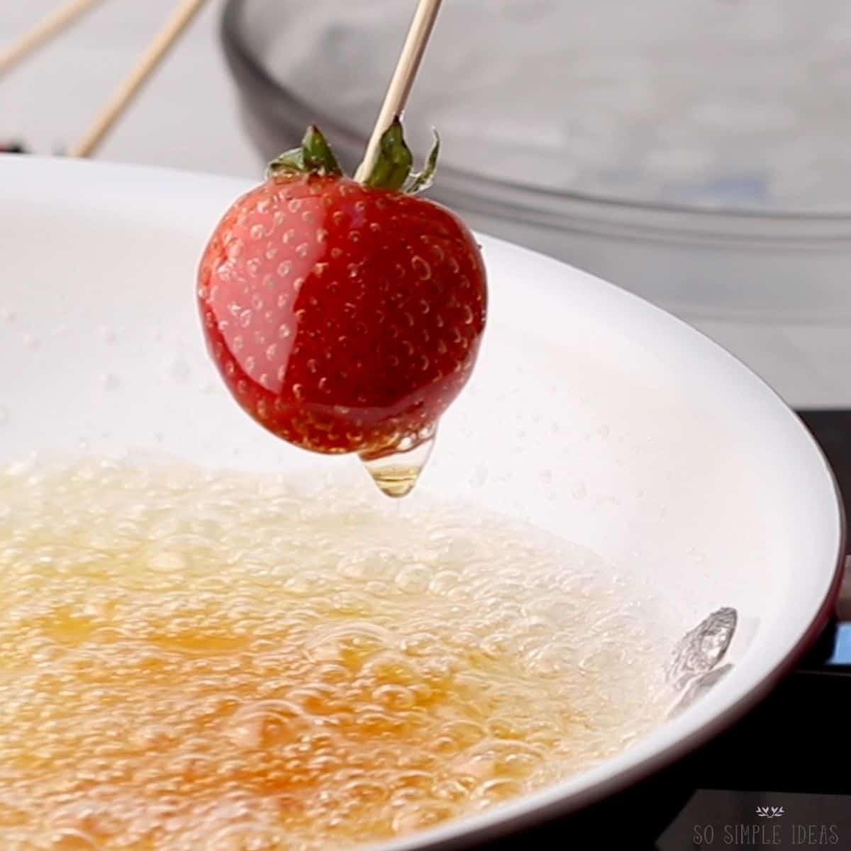 removing skewered strawberry from hot candy syrup.