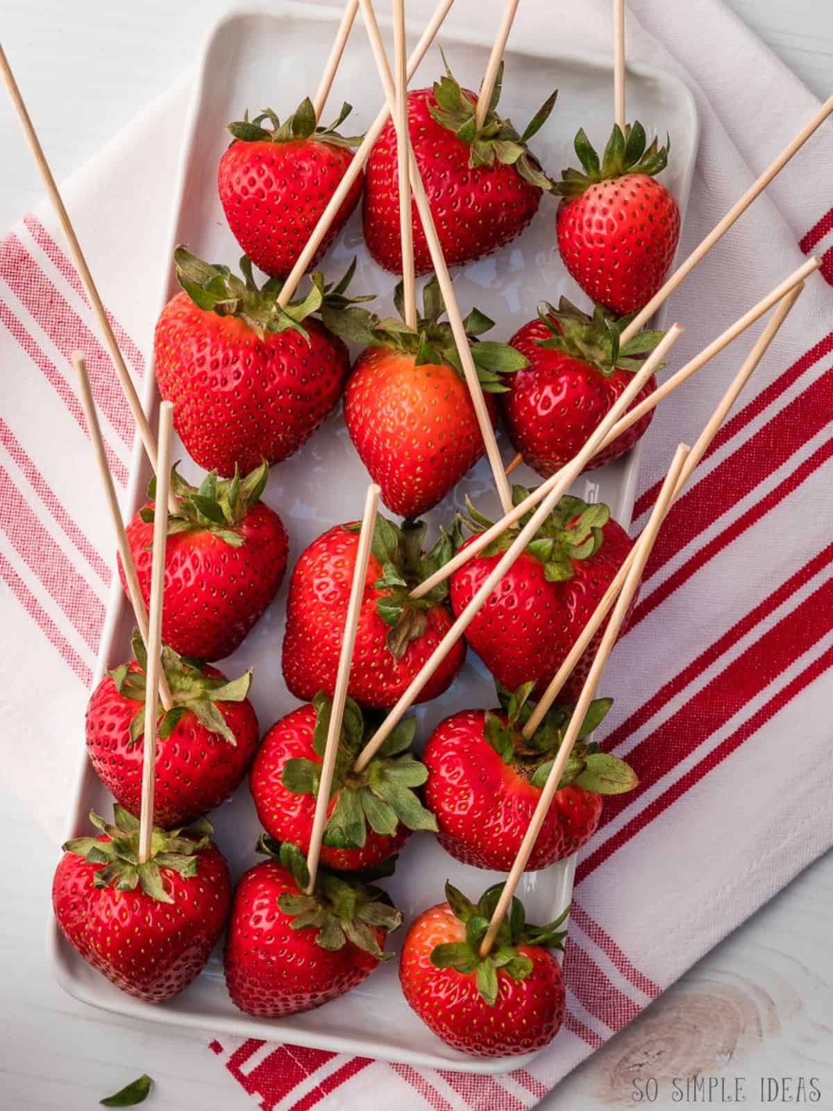 skewered strawberries on a white rectangular plate.