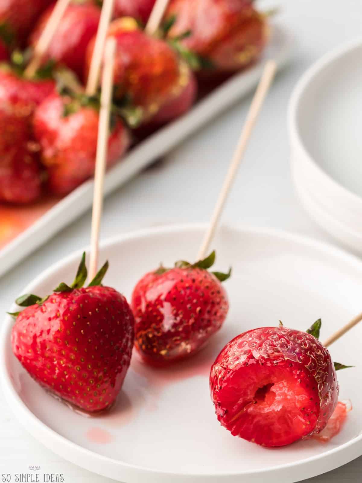 serving of strawberry tanghulu on small rimmed plate with one bitten.