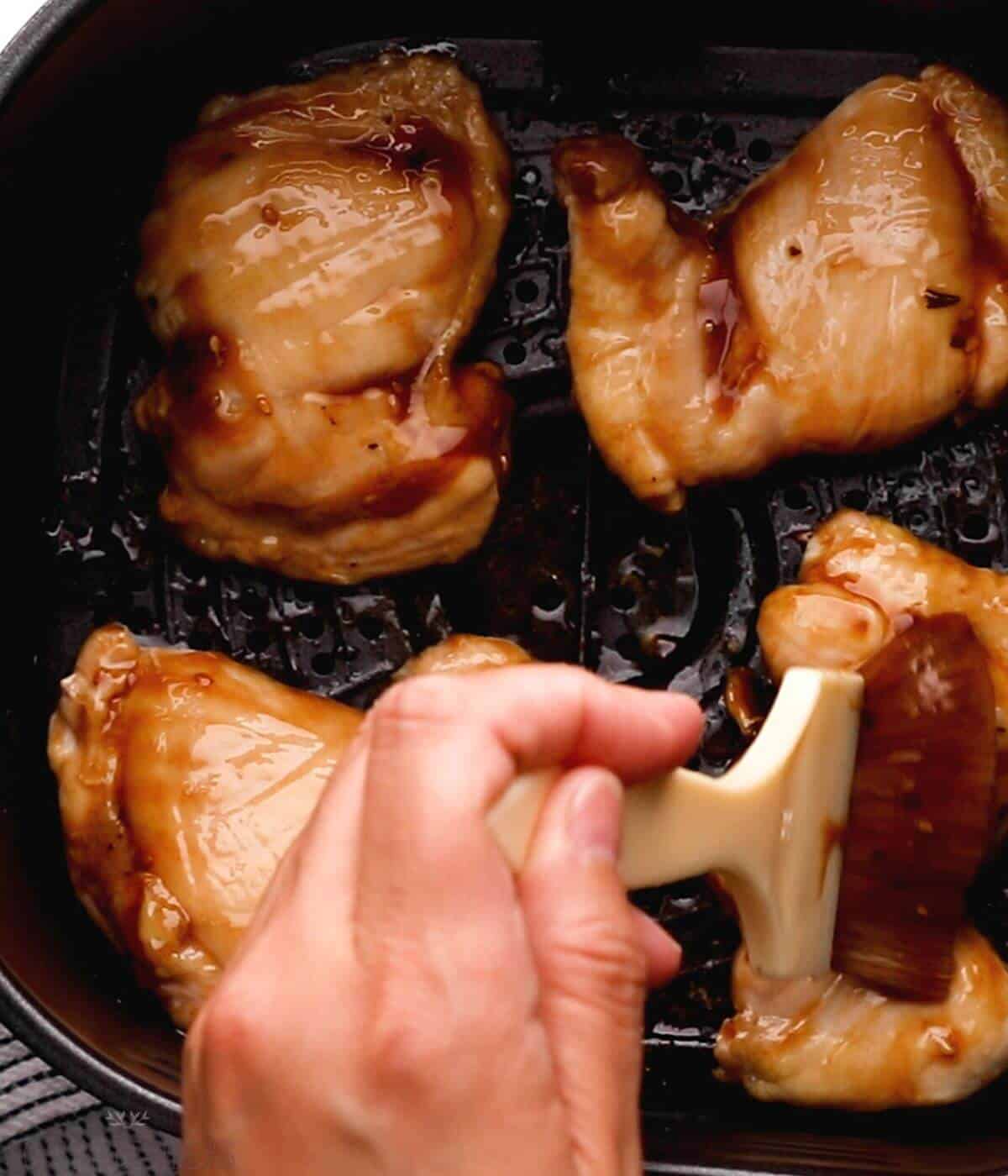 brushing teriyaki sauce over chicken in air fryer basket.