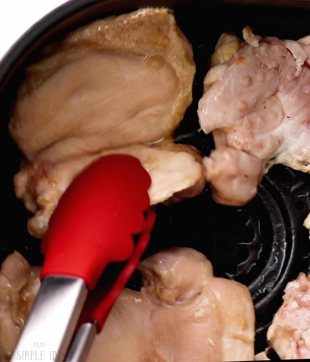 flipping chicken piece in air fryer basket.