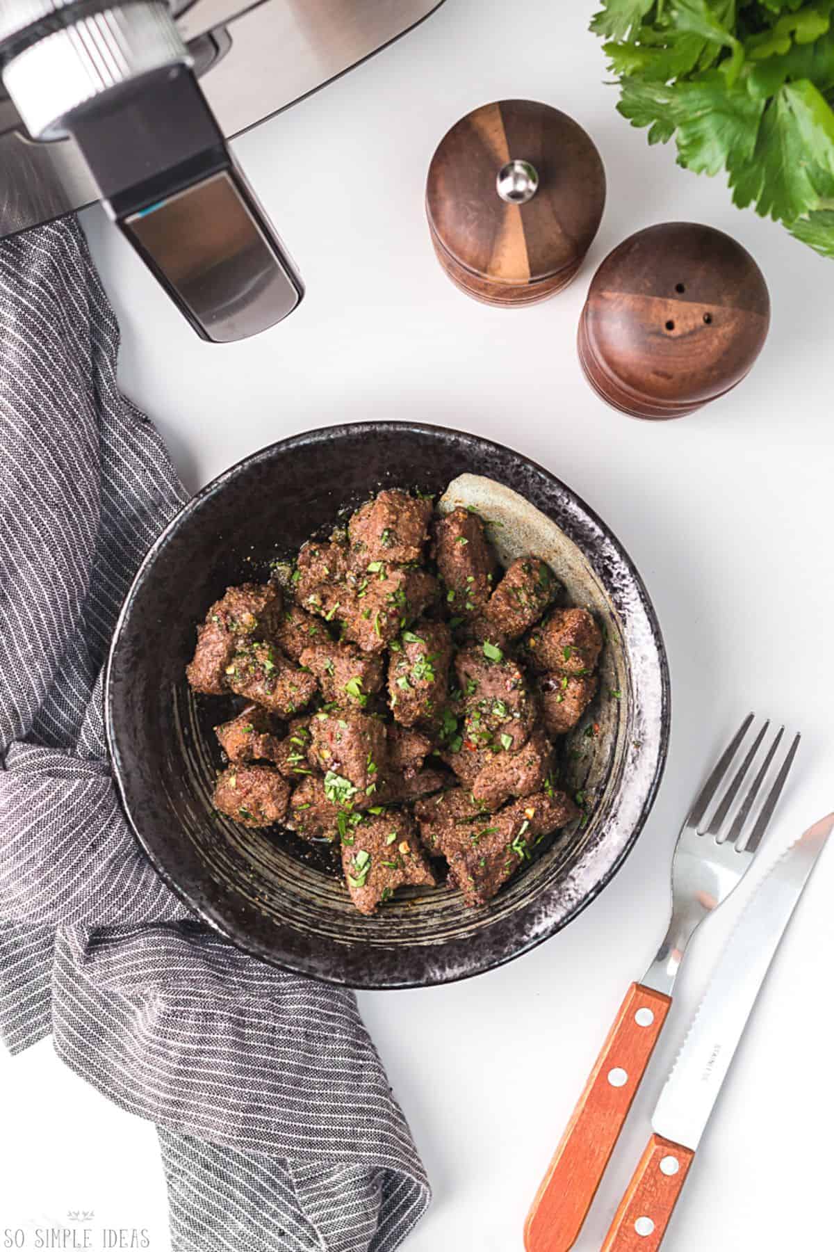 garnished steak tips in black bowl.