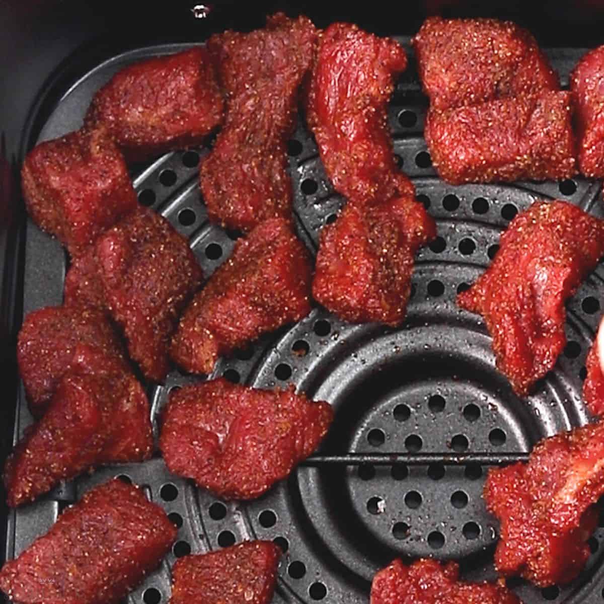 raw seasoned steak tips in air fryer basket.