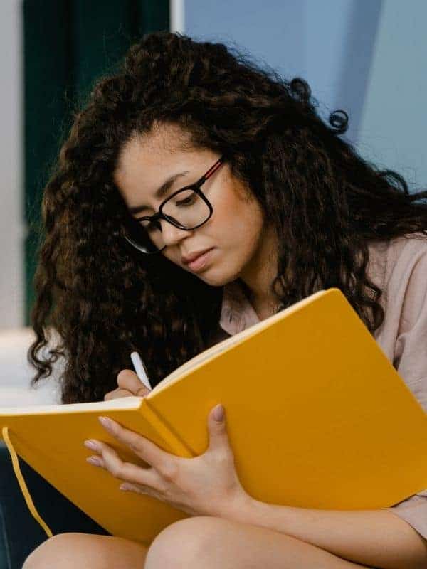 writing in a large orange journal.