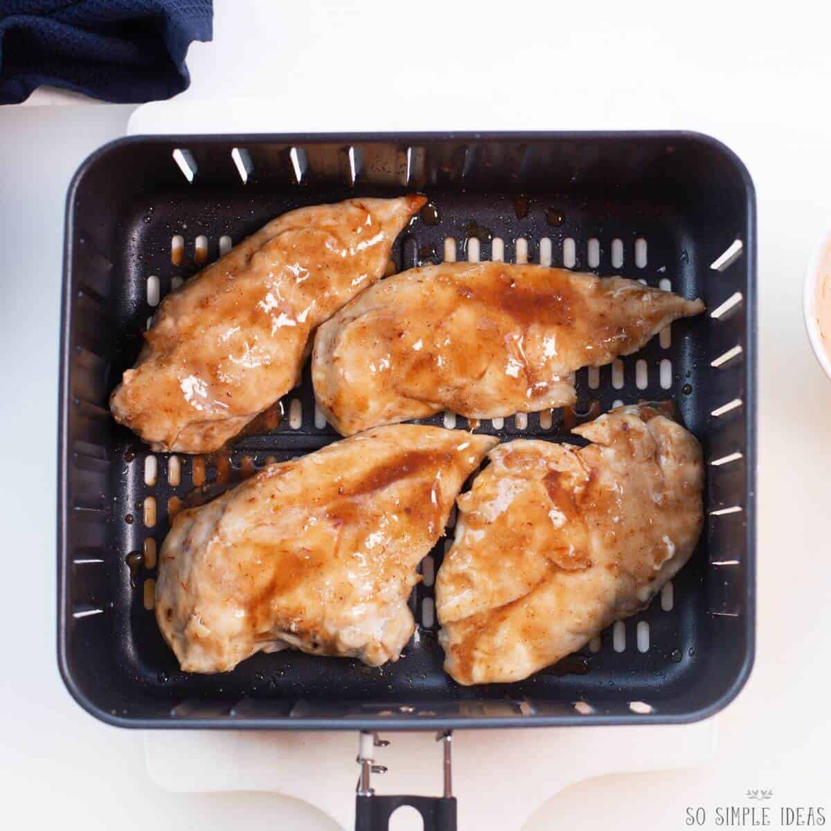 adding sauce to breast meat in air fryer basket.