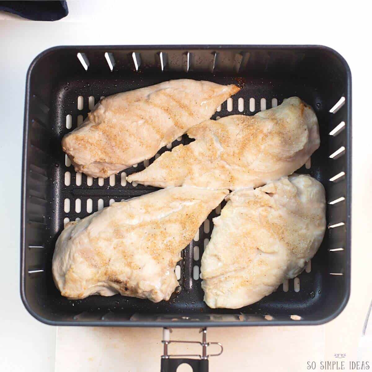 half cooked chicken in air fryer basket.