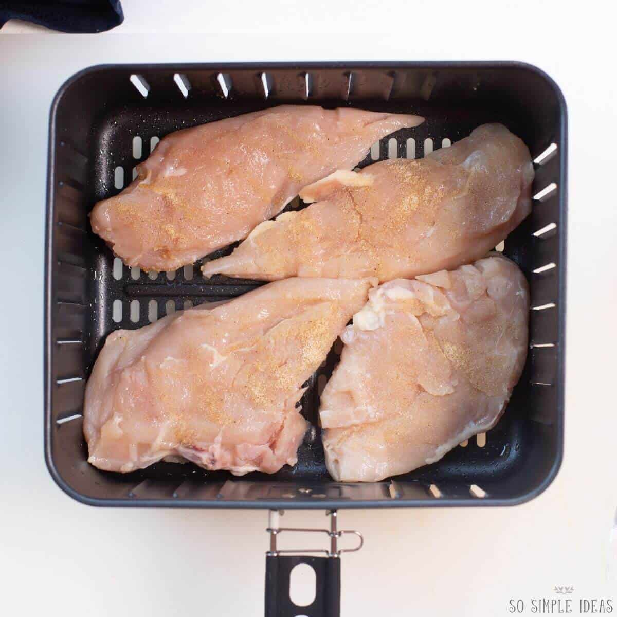 seasoned chicken breasts in air fryer basket.